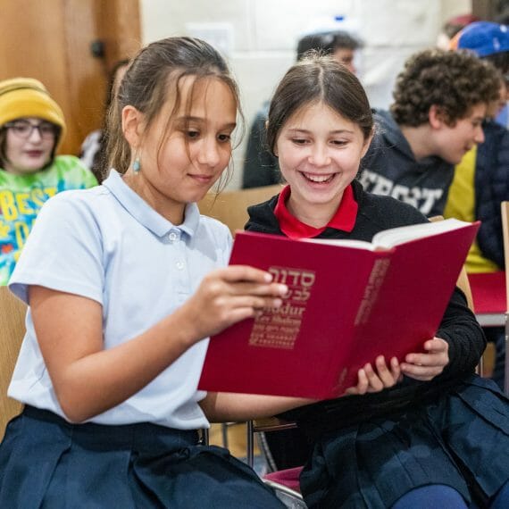 two young girls reading book together